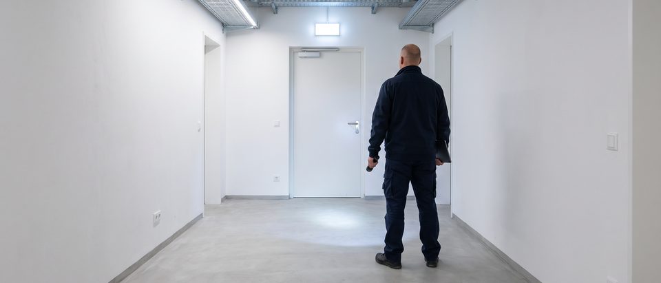 Hausbetreuer prüft mit einer Taschenlampe einen freien Fluchtweg im Kellergang