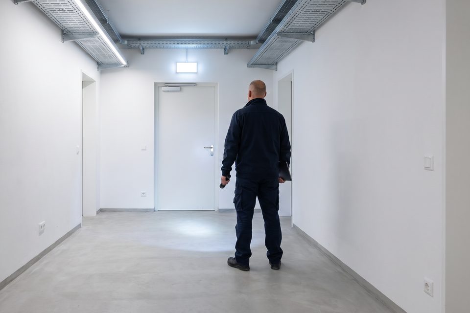 Hausbetreuer prüft mit einer Taschenlampe einen freien Fluchtweg im Kellergang